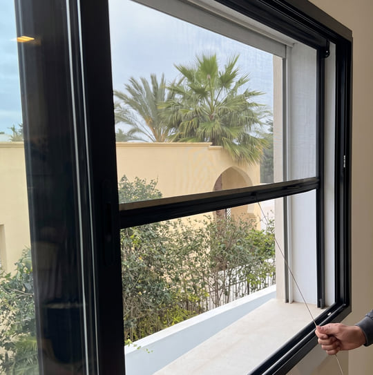 Moustiquaire aluminium rétractable abaissée sur une fenêtre donnant sur un jardin à Tanger — Aluminium Tanger